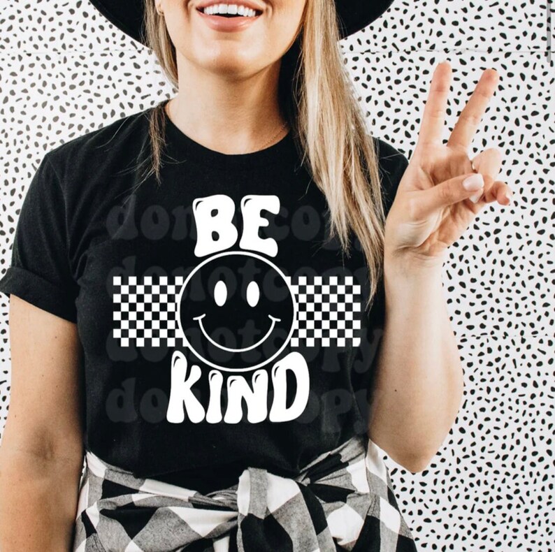 May include: Black t-shirt with a white smiley face and checkered pattern. The text "BE KIND" is written in white letters.