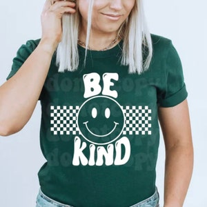 May include: A green t-shirt with a white smiley face and the words "BE KIND" in a retro font. The smiley face is surrounded by a black and white checkered pattern.