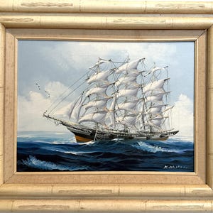 May include: Oil painting of a tall ship sailing on a blue ocean under a cloudy sky. The ship has white sails and a black and brown hull. The painting is in a bamboo-style frame.