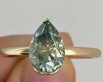 May include: A gold ring featuring a pear-shaped, light green gemstone. The ring has a simple, elegant design with a thin band. The logo "ORRA LUXE LAB-GROWN JEWELRY" is visible in the background.