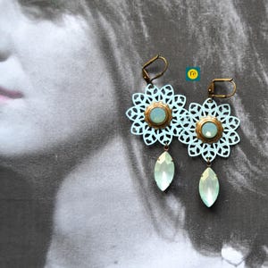 Pode incluir: Um par de brincos azuis claros com um delicado design floral e um pingente de cristal em forma de lágrima.