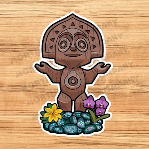 May include: A sticker featuring a cartoon wooden tiki statue with outstretched arms. The statue is brown with a detailed headpiece and a central design. It stands on a bed of blue stones with a yellow flower and purple orchids.