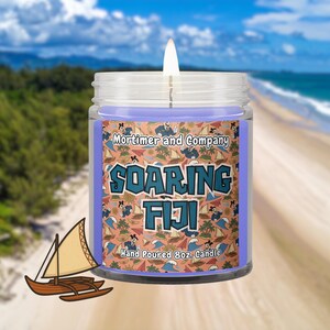May include: A clear glass jar candle with light purple wax and a lit wick. The label features a peach background with a repeating pattern of cartoon characters, sailboats, and waves, with the text Mortimer and Company SOARING FIJI Hand Poured 227g Candle.