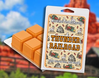 May include: Orange wax melts in a white plastic container with the text "Thunder Railroad". The packaging features a cartoon design with a train, goat, and mountain. The wax melts are in a tray with four cubes.