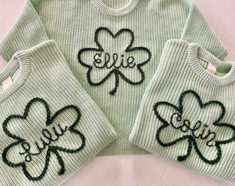 May include: Three green knitted sweaters with black embroidered shamrocks and names "Ellie", "Julia", and "Colin".