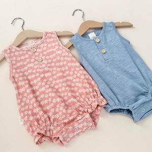 May include: Two sleeveless baby onesies, one with a floral print in pink and white and the other in a solid light blue.