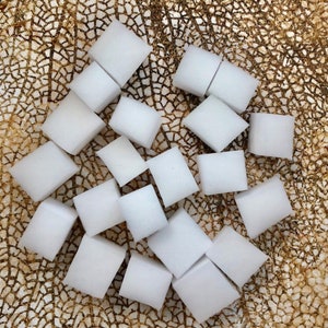 May include: A pile of white, square-shaped sponges on a gold and brown textured surface.