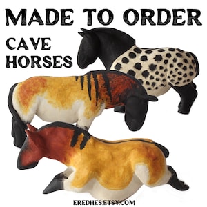 Puede incluir: Tres esculturas de caballos de las cavernas hechas a mano en varios colores. Un caballo es negro y blanco moteado, otro es marrón con rayas negras y el tercero es rojo y marrón. El texto "MADE TO ORDER" y "CAVE HORSES" está en la parte superior.