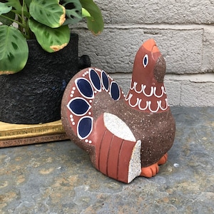 May include: A brown ceramic figurine of a stylized bird with white and blue painted details. The bird has a long neck and a rounded body with a tail that is spread out behind it.