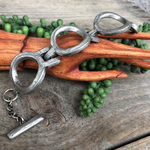 May include: A silver metal bracelet with a chain and a bar. The bracelet is made of three connected rings, each with a different shape.