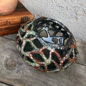 May include: A ceramic bowl with a unique, intricate design. The bowl is made of a dark green glaze with brown accents, creating a web-like pattern. The bowl is perfect for displaying small items or holding trinkets.