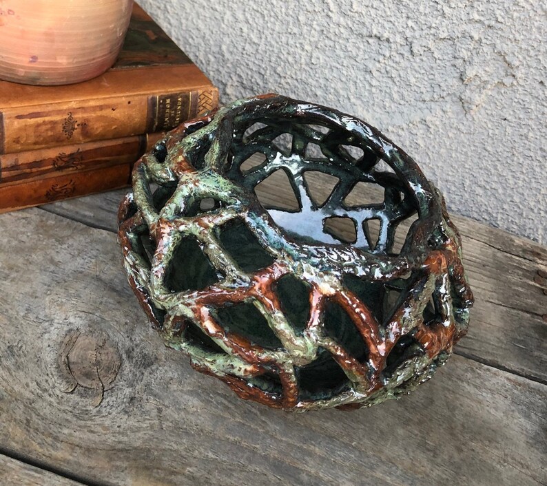 May include: A ceramic bowl with a unique, intricate design. The bowl is made of a dark green glaze with brown accents, creating a web-like pattern. The bowl is perfect for displaying small items or holding trinkets.