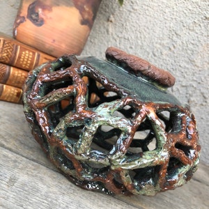 May include: A ceramic vase with a brown and green glaze. The vase has a lattice design and a textured surface.