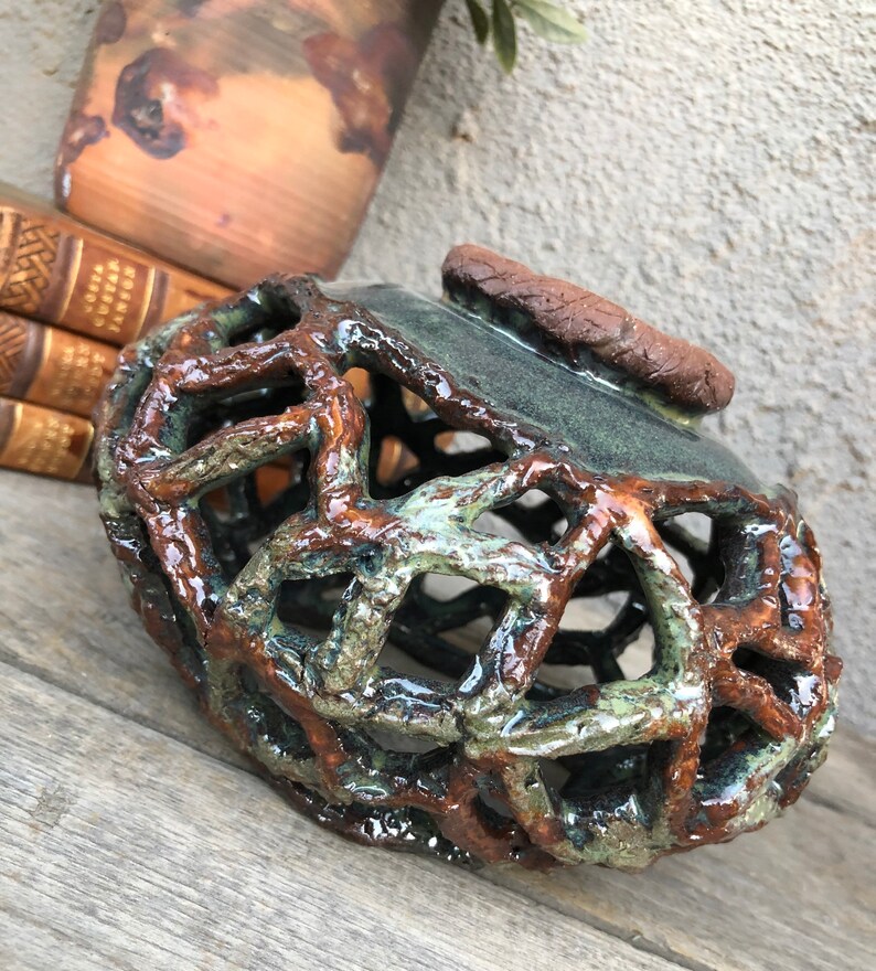 May include: A ceramic vase with a brown and green glaze. The vase has a lattice design and a textured surface.
