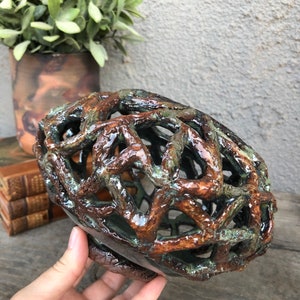 May include: A ceramic bowl with a brown and green glaze. The bowl is made of a latticework design and has a unique, organic shape.