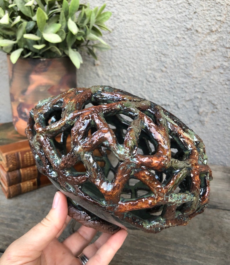 May include: A ceramic bowl with a brown and green glaze. The bowl is made of a latticework design and has a unique, organic shape.
