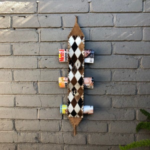 May include: A white and black cowhide magazine rack with five magazines inserted. The rack is hanging on a gray brick wall.