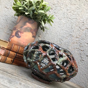 May include: A ceramic bowl with a unique, open-weave design. The bowl is glazed in shades of brown, green, and blue, giving it a rustic and earthy look.