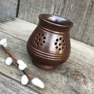 May include: A brown ceramic incense burner with a decorative pattern of holes. The burner has a rounded base and a wide opening at the top.