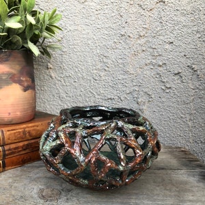 May include: A ceramic vase with a unique, intricate design resembling a woven basket. The vase is brown and green with a glossy finish.