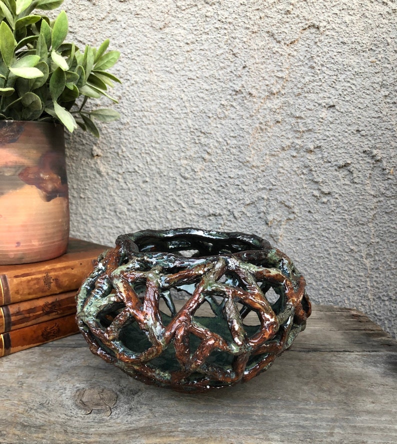 May include: A ceramic vase with a unique, intricate design resembling a woven basket. The vase is brown and green with a glossy finish.
