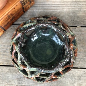 May include: A ceramic bowl with a green glaze and a brown, twig-like design. The bowl is handmade and has a unique, rustic look.