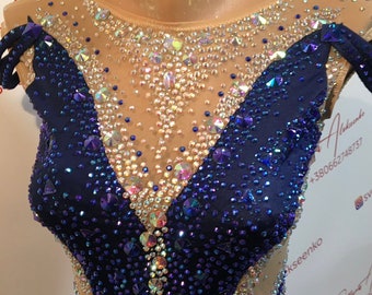 Può includere: Un body blu navy ornato da numerosi strass iridescenti, con scollatura e maniche trasparenti. Il corpetto presenta un design a scollo a V e intricati motivi di cristallo. Questo capo è probabilmente per la ginnastica o la danza.
