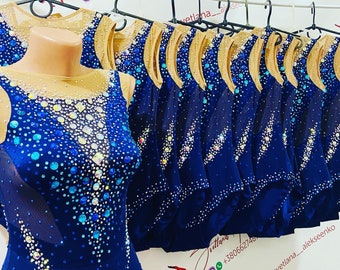 May include: A row of navy blue leotards with a sheer mesh overlay and embellished with rhinestones in various shades of blue and gold. The leotards are hanging on hangers.