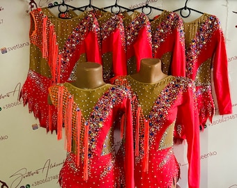 May include: Six red leotards with long sleeves and a V-neckline. The leotards are decorated with rhinestones, sequins, and fringe. The leotards are hanging on hangers.