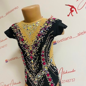 Pu&ograve; includere: Body nero e nude per ginnastica ritmica, impreziosito da strass scintillanti di vari colori. Il body presenta maniche corte e scollatura alta, con un motivo decorativo di cristalli. Il design include un pannello in rete.