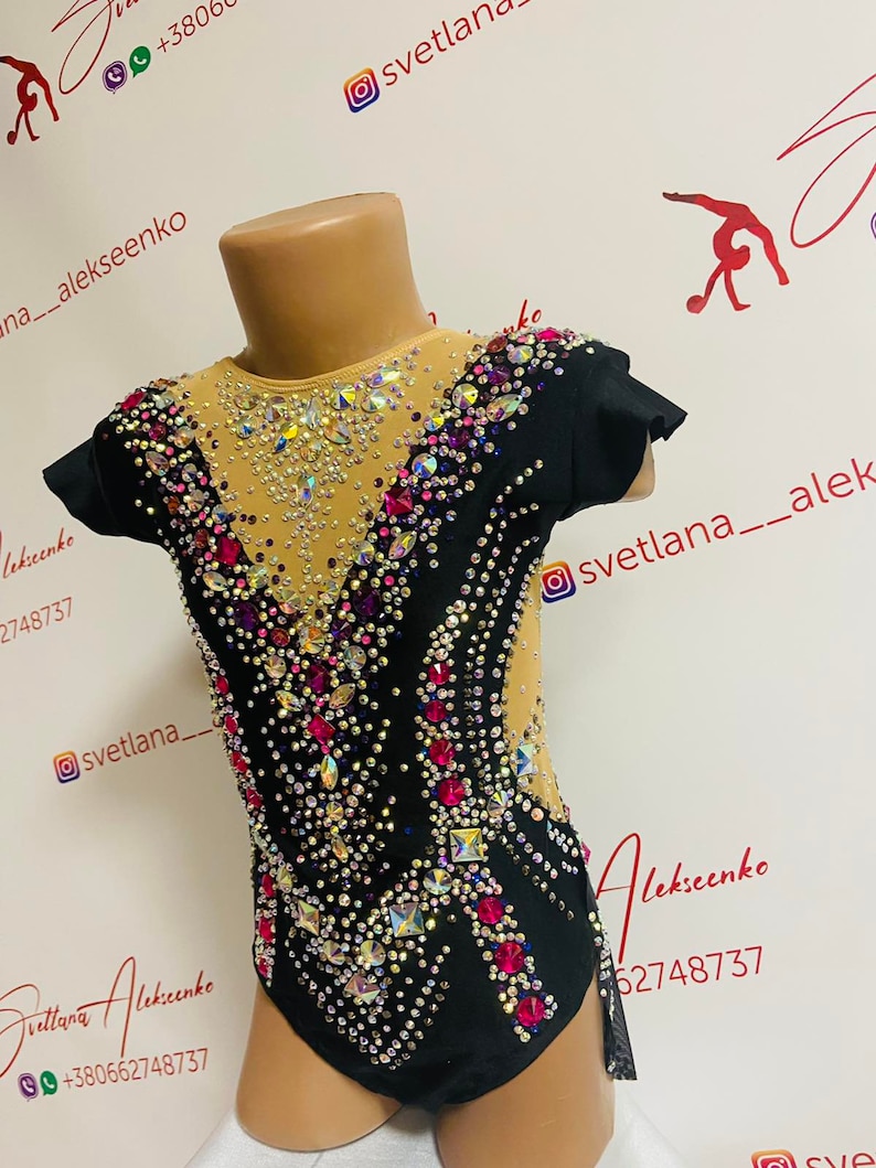 Pu&ograve; includere: Body nero e nude per ginnastica ritmica, impreziosito da strass scintillanti di vari colori. Il body presenta maniche corte e scollatura alta, con un motivo decorativo di cristalli. Il design include un pannello in rete.
