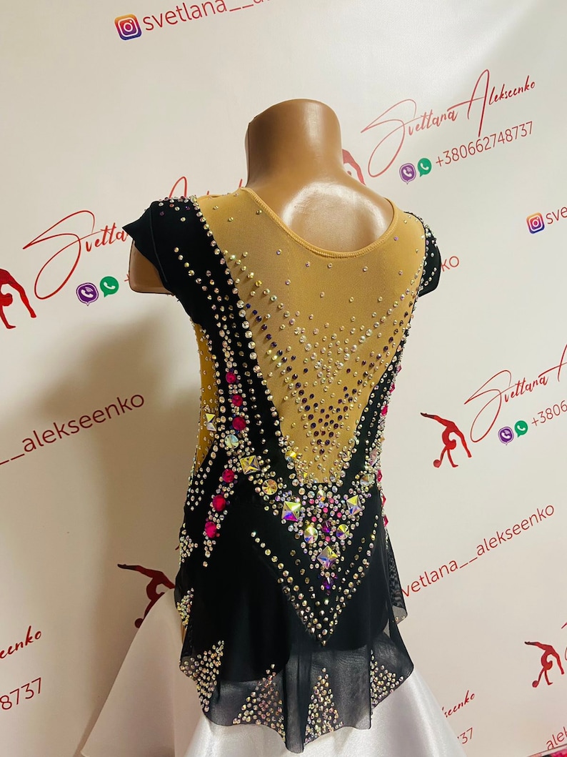 Pu&ograve; includere: Un body nero e bianco con schiena e maniche in rete nude trasparente. Il body &egrave; impreziosito da strass e gemme colorate. Il design presenta un motivo a forma di V sul davanti e sul retro, con una gonna bianca.