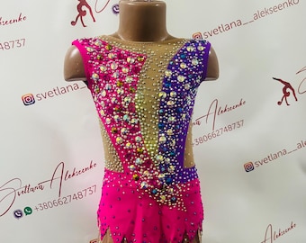 Peut inclure: Un justaucorps rose et violet avec des strass et une couronne sur un mannequin. Le justaucorps a un col en V et une jupe. Le justaucorps est décoré de strass de différentes couleurs, notamment rose, violet, bleu et transparent. La couronne est dorée et a un design rose et violet.