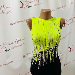 Puede incluir: Maillot sin mangas, amarillo neón y negro, con cuello redondo. El corpiño está adornado con un patrón de pequeños pedrería brillantes. El maillot se exhibe en un maniquí.