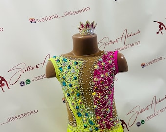 May include: A bright yellow leotard with pink and green accents, adorned with rhinestones and fringe. The leotard has a sleeveless design and a high neckline. The leotard is worn by a mannequin with a crown on its head.