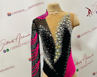 May include: A black leotard with pink and black mesh sleeves. The leotard is decorated with rhinestones and has a V-neckline. The leotard is on a mannequin.