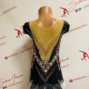 Pu&ograve; includere: Body nero e beige con abbellimenti di cristalli e strass. Il body ha una parte superiore in rete beige trasparente, maniche corte nere e una gonna nera con sottogonna bianca. Il design presenta un motivo geometrico.