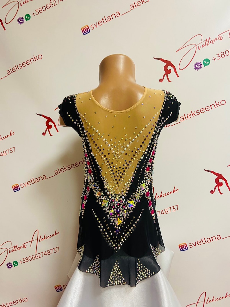 Pu&ograve; includere: Body nero e beige con abbellimenti di cristalli e strass. Il body ha una parte superiore in rete beige trasparente, maniche corte nere e una gonna nera con sottogonna bianca. Il design presenta un motivo geometrico.