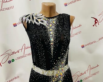May include: A black leotard with a silver trim and rhinestones. The leotard has a mesh design and a large rhinestone design on the front. The leotard is on a mannequin.