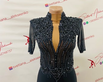 May include: A black, beaded, long-sleeved leotard with a plunging neckline and a sheer mesh overlay. The leotard has a fitted bodice and a skirt that flows to the floor. The leotard is decorated with black beads and rhinestones.