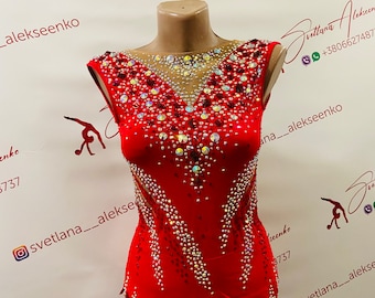 May include: A red leotard for rhythmic gymnastics, adorned with sparkling rhinestones and crystals. The sleeveless garment features a high neckline and a unique, asymmetrical skirt design. The leotard is displayed on a mannequin.