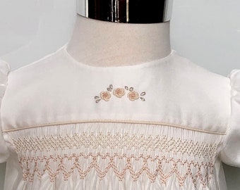 May include: White baby dress with a delicate floral embroidery design and a smocked bodice.