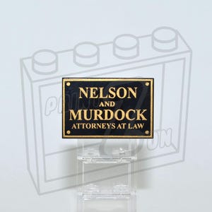 May include: Black sign with gold lettering that reads "Nelson and Murdock Attorneys at Law". The sign is on a clear plastic stand.