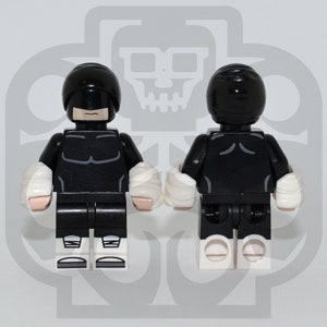 May include: Black and white Lego minifigure with a black mask and white bandages on the arms. The minifigure is standing on a white surface.