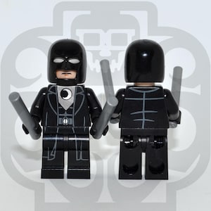 Könnte beinhalten: Eine schwarze Lego-Minifigur mit Maske und Anzug, die zwei graue Stäbe hält. Die Minifigur hat einen weißen Halbmond auf der Brust. Die Rückseite der Minifigur zeigt ein skelettartiges Design.