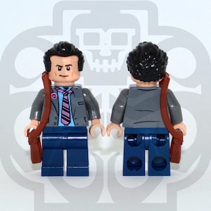 Może przedstawiać: Lego minifigurka przedstawiająca osobę w szarej marynarce, niebieskiej koszuli z różowo-białym paskowanym krawatem, niebieskich spodniach i brązowych butach. Minifigurka trzyma brązową teczkę. Minifigurka jest pokazana z przodu i z tyłu.