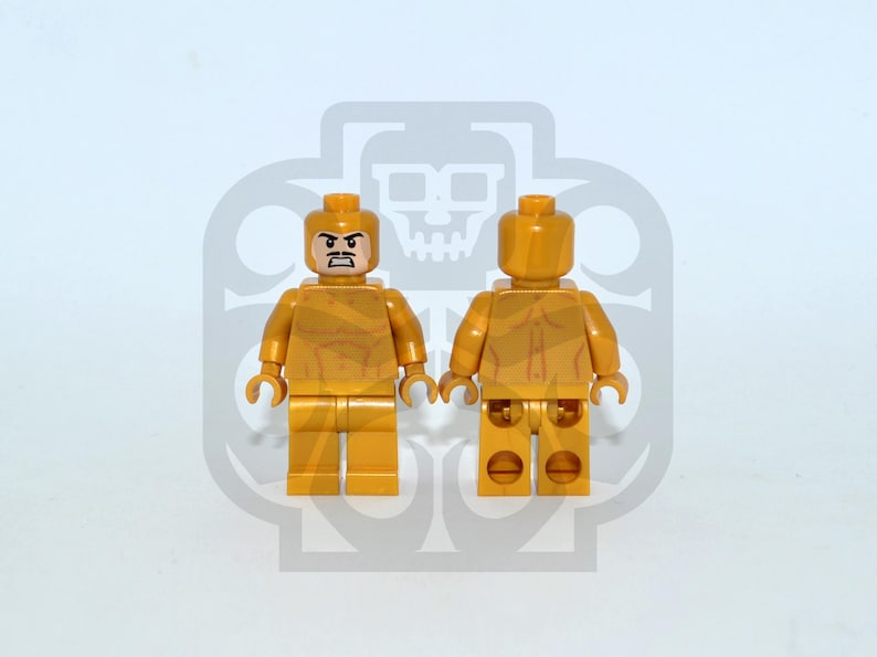 Op de afbeelding: Twee goudkleurige Lego-minifiguren, &eacute;&eacute;n naar voren en de andere naar achteren gericht. De figuur aan de voorkant heeft een streng gezicht met een snor. Beide figuren hebben gedetailleerde torso- en beenontwerpen. De achtergrond is lichtgrijs met een logo.