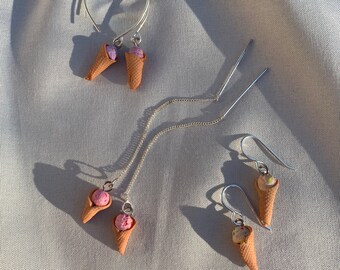 May include: Three pairs of dangle earrings featuring miniature ice cream cones with different colored ice cream. The earrings are made of silver and have a delicate chain.