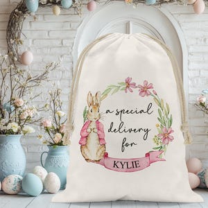 May include: A white canvas bag with a pink bunny rabbit illustration and floral design. The bag has the text "a special delivery for KYLIE" printed on it.