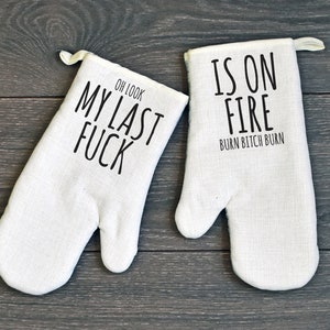 May include: A pair of white oven mitts with black text. One mitt says "Oh Look My Last Fuck" and the other says "Is On Fire Burn Bitch Burn".